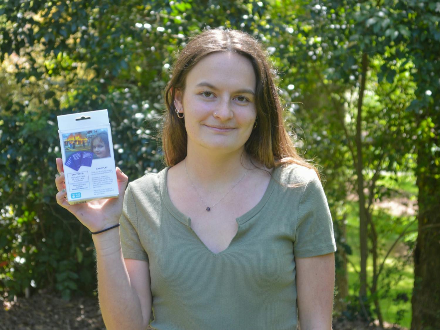 Zoe Roth, a senior peace war and defense major and subject of the meme 'Disaster Girl', holds up the card game What Do You Meme? on Tuesday Apr 13, 2021 in Chapel Hill.