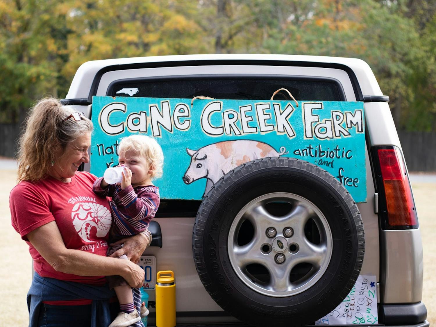 Eliza Maclean, owner of Cane Creek Farm, stands with Watt Basnight, 1, whom she co-parents, at the Carrboro Farmer's Market on Wednesday, Oct. 26, 2022.