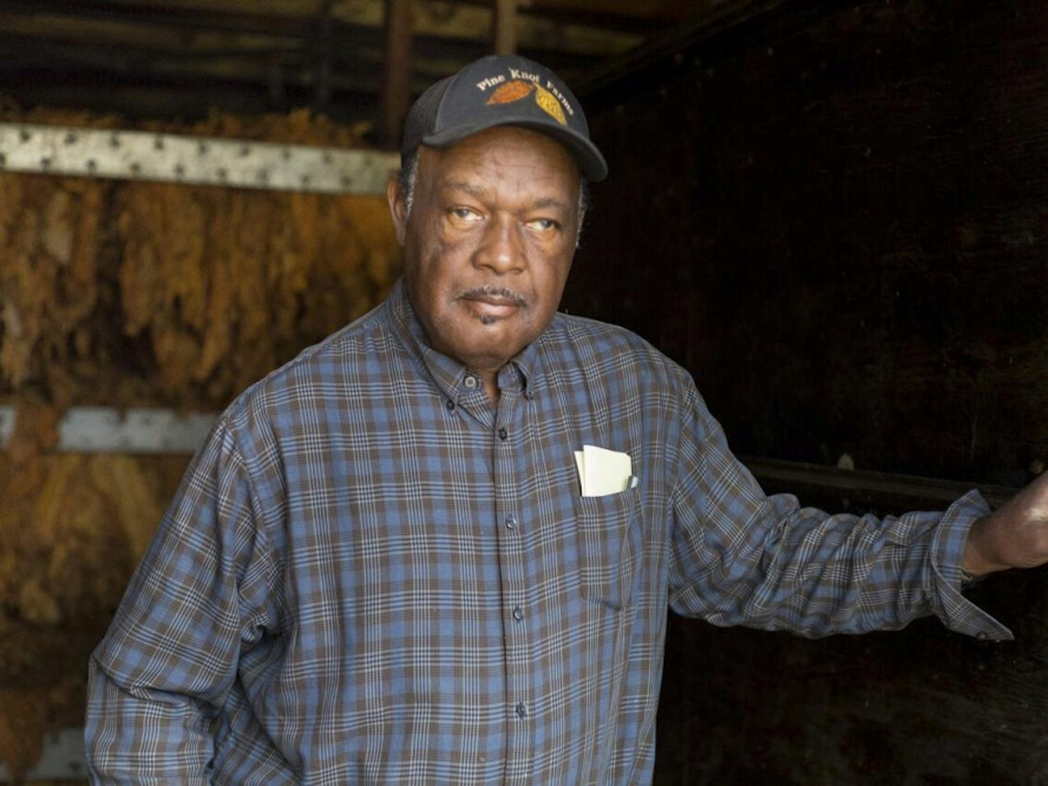 Stanley Hughes poses for a portrait in front of tobacco drying racks at Pine Knot Farms on Monday.