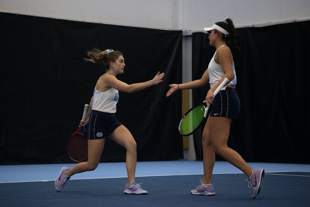 <p>Junior Fiona Crawley high-fives sophomore Carson Tanguilig during their doubles match against Elon University at the Cone-Kenfield Tennis Center on &nbsp;Friday, Jan. 13, 2023. UNC beat Elon 4-2.</p>