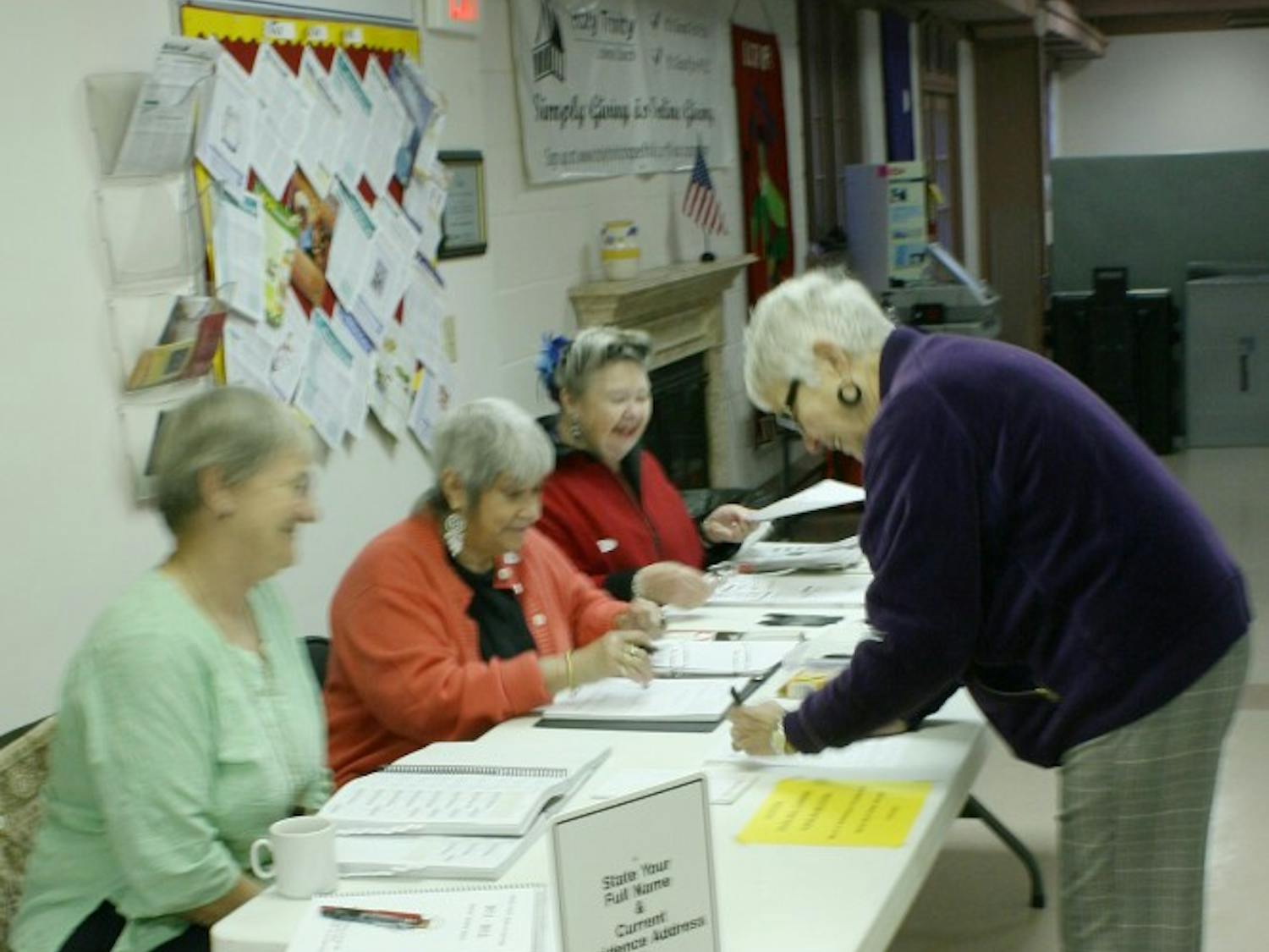 left to right: Iris Schwintzer, Shirley Ray, Ernie Quade. Judges for the E Franklin Street Precinct assist morning voters. Deborah Finn, of 214 Hillsborough St., votes with her husband and dog. (purple jacket). At larger elections, Mrs. Finn is also a judge for the E Franklin Street Precinct