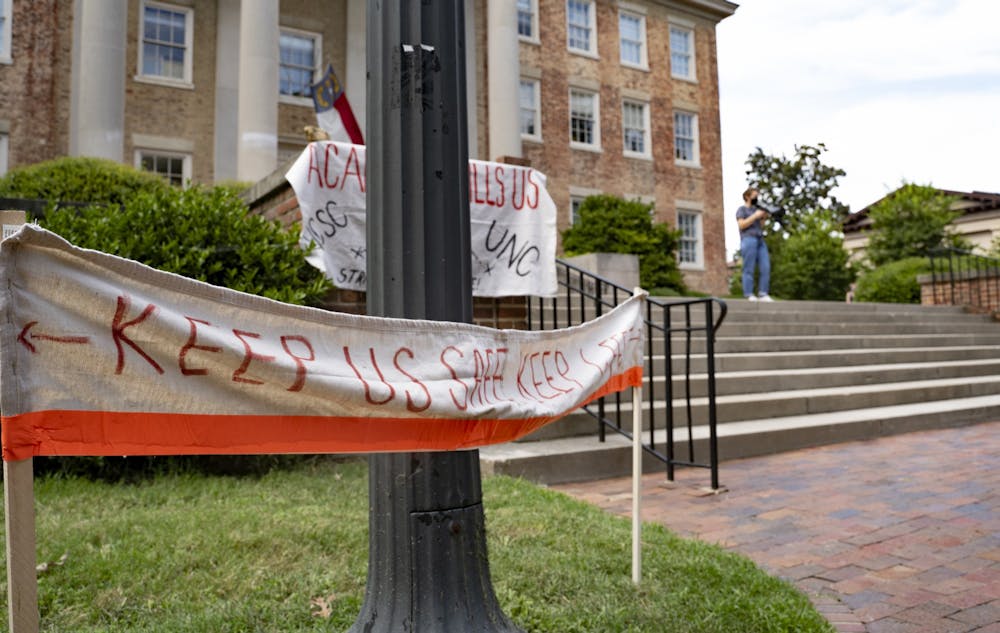 <p>Signs promoting social distancing and safety at the Die-In Protest on Wednesday, Aug. 5, 2020 as Jennifer Standish, a UNC graduate student in the Department of History, speaks outside of South Building on Wednesday, Aug. 5, 2020. The protest called for UNC to transition to fully remote classes for the Fall 2020 semester after a letter of caution sent to Chancellor Guskiewicz by the Orange County Health Director Quintana Stewart.</p>