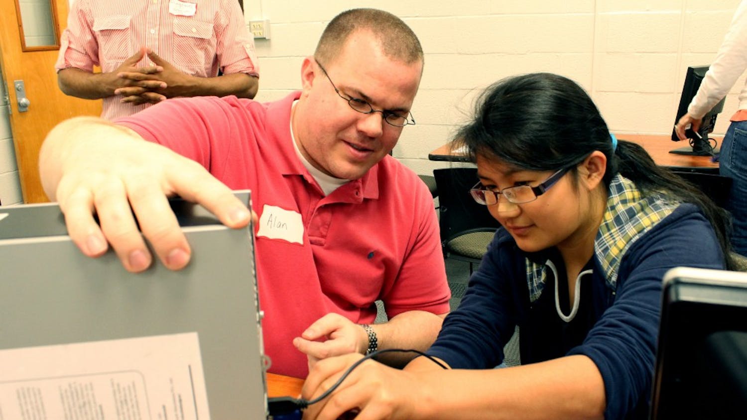 Hla Win Tway, a 8th Grader/15 years old girl studying at Smith Middle School, is connecting the monitor to the main body under the instruction of the volunteer, Mr. Alan Brown, who is a technical specialist for Northside Elementary School. He lives in Morrisville. 