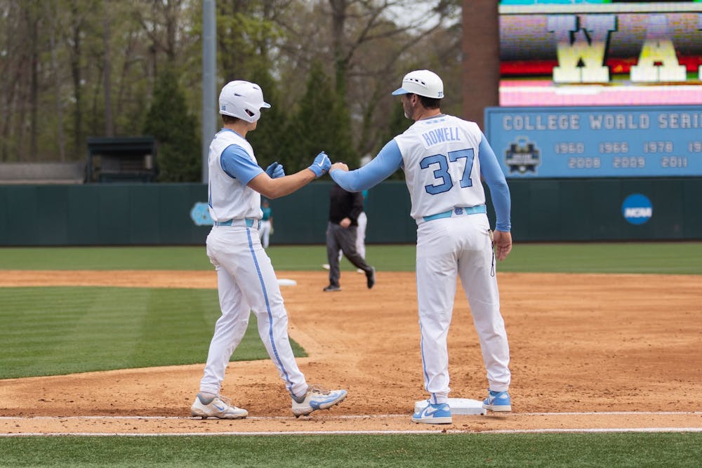 UNC redshirt first-year Casey Cook (16) fist-bumps assistant coach Jason Howell (37) after making it to first base during the baseball game against Costal Carolina on Tuesday, March 27, 2023, at Boshamer Stadium. UNC fell to Costal Carolina 7-12.