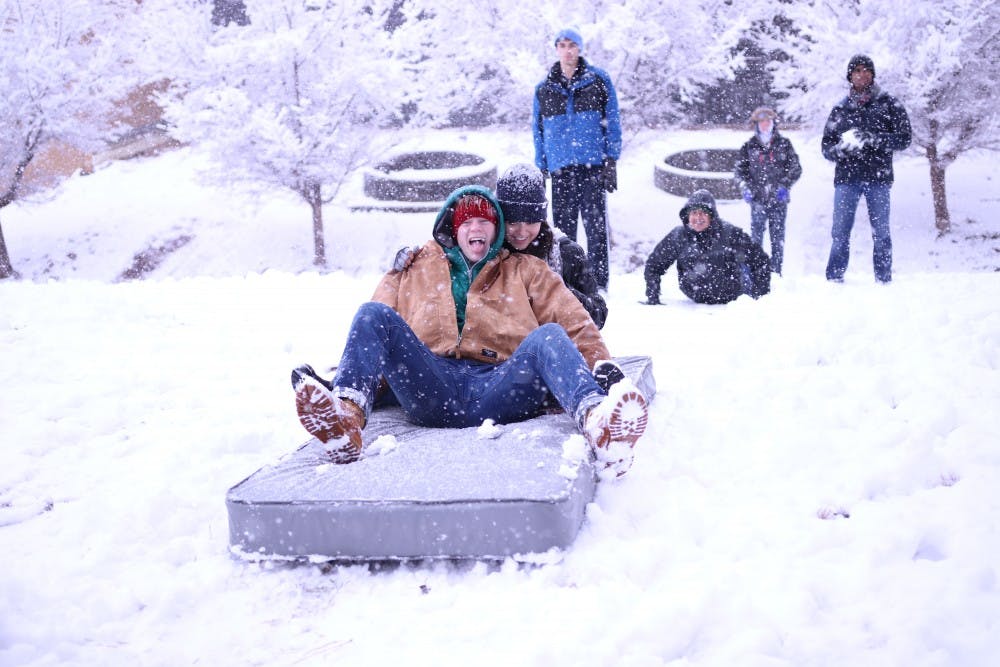 <p>First-years Grantito Everist (left) and Cat Chang (right) use a mattress to sled down the hill at the Dean Smith Center during Wednesday's snowstorm.</p>