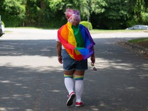 DTH Photo Illustration. A person walks down a street wearing a pride flag.