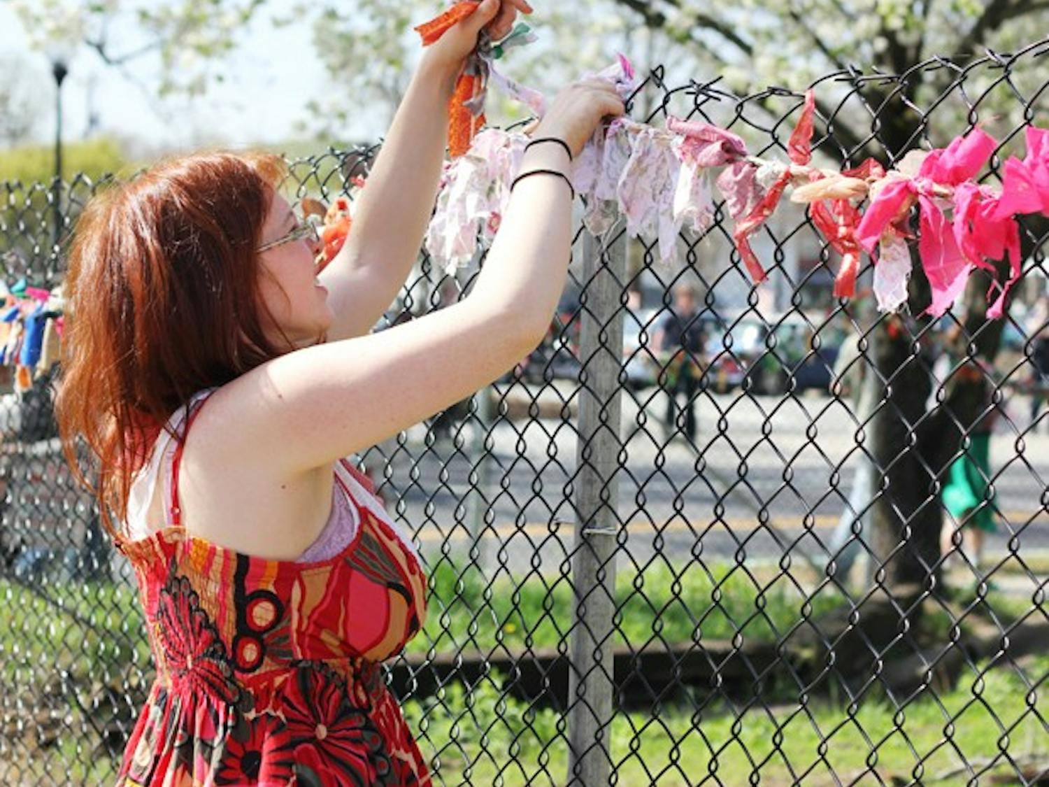 Candace Burch decorates the fence surrounding the lot 201 N. Greensboro St. with a garland made of up-cycle materials at the Guerrilla Gardening event in Carrboro Saturday morning at the Carrboro Commune. The group gardened and decorated around the lot to protest the proposed CVS store.