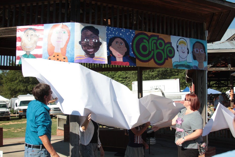 Mural artist Michael Brown (far left) and Carrboro Elementary School teacher Deb Cox (far right) help unveil a replica of the mural at the dedication ceremony in the Carrboro Town Commons on Saturday.