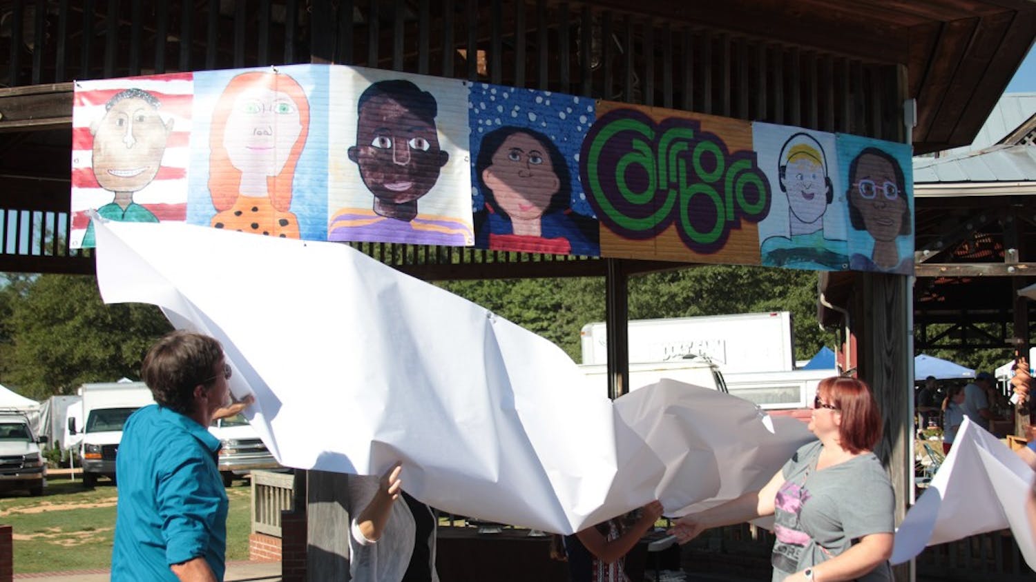 Mural artist Michael Brown (far left) and Carrboro Elementary School teacher Deb Cox (far right) help unveil a replica of the mural at the dedication ceremony in the Carrboro Town Commons on Saturday.