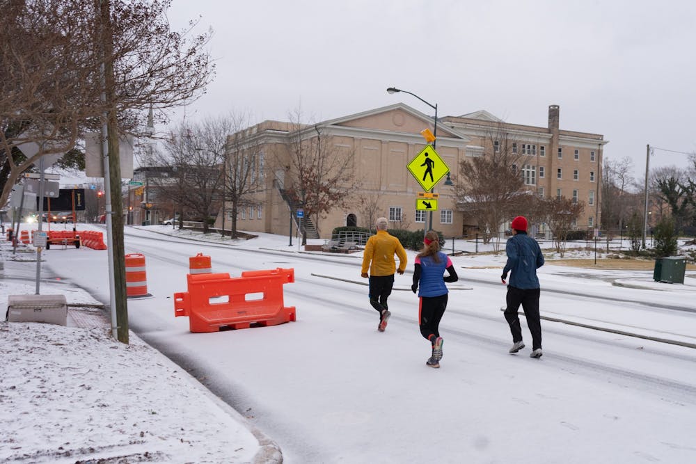 A group of people run in the snow on Franklin Street in Chapel Hill on Sunday, Jan. 16, 2022.