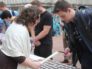 Rabbi Melissa B. Simon (left) helps Maximilian Jeremy Bazil, a sophomore biology major, (right) light a candle in honor of the victims of the Pittsburg synagogue shooting at the Hillel Stand Together Against Hate Solidarity Gathering in front of the Student Union on Thursday, Nov. 1, 2018.