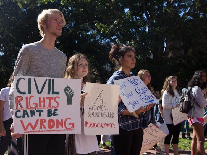 (From left to right) Riley Curtis, Reiley Baker, and Amy Estrada stand in the front of the crowd at South Building during the Believe Surivors Rally Friday, Oct. 12, 2018. Demonstrators gathered at South Building to hear testimonies and  proceed to march to fraternity court in support of survivors of sexual harrassment and assault.