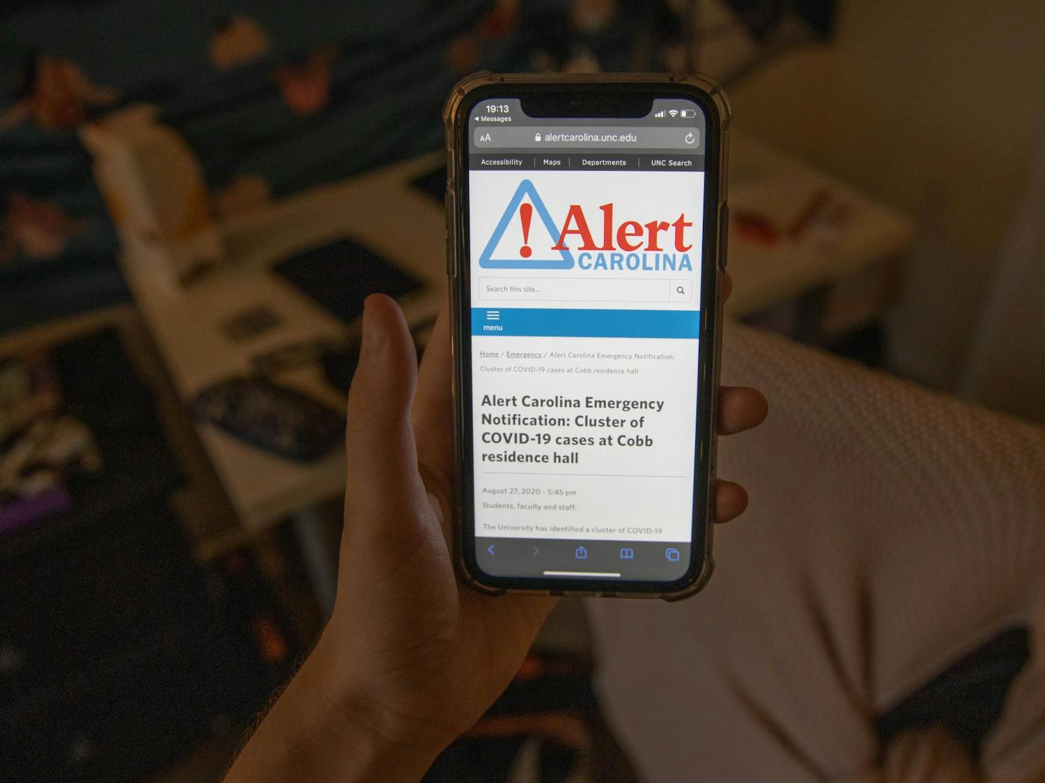 DTH Photo Illustration. A student looks at the latest Alert Carolina notification about a cluster at Cobb Resident Hall. The university will no longer send Alert Carolina notifications about clusters on campus, UNC announced on Friday, Aug. 28, 2020.
