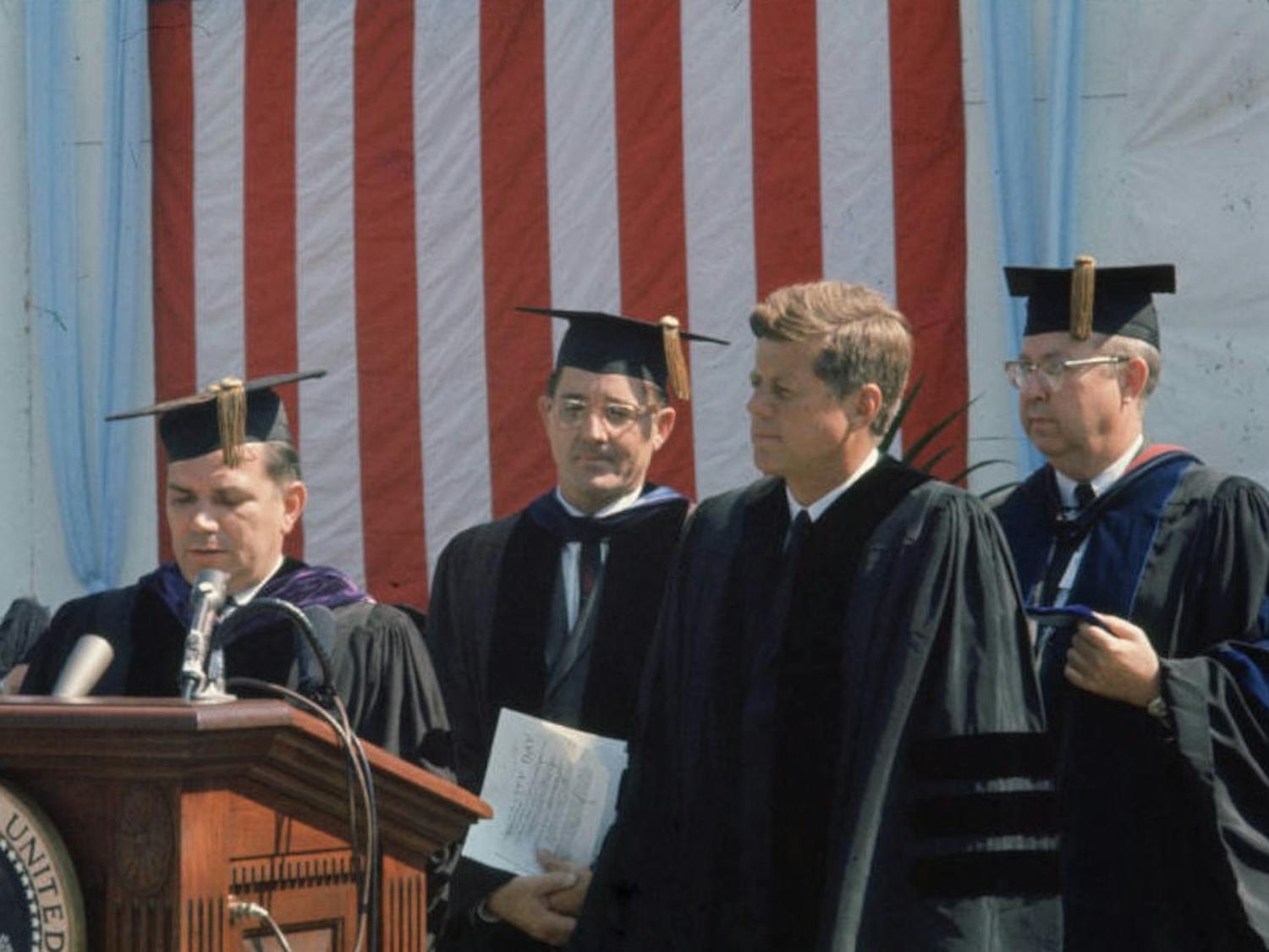 UNC Chancellor William Aycock pictured speaking at podium, with UNC System President Bill Friday, President John F. Kennedy, and distinguished professor James L. Godfrey at University Day, October 12, 1961 at UNC Chapel Hill.