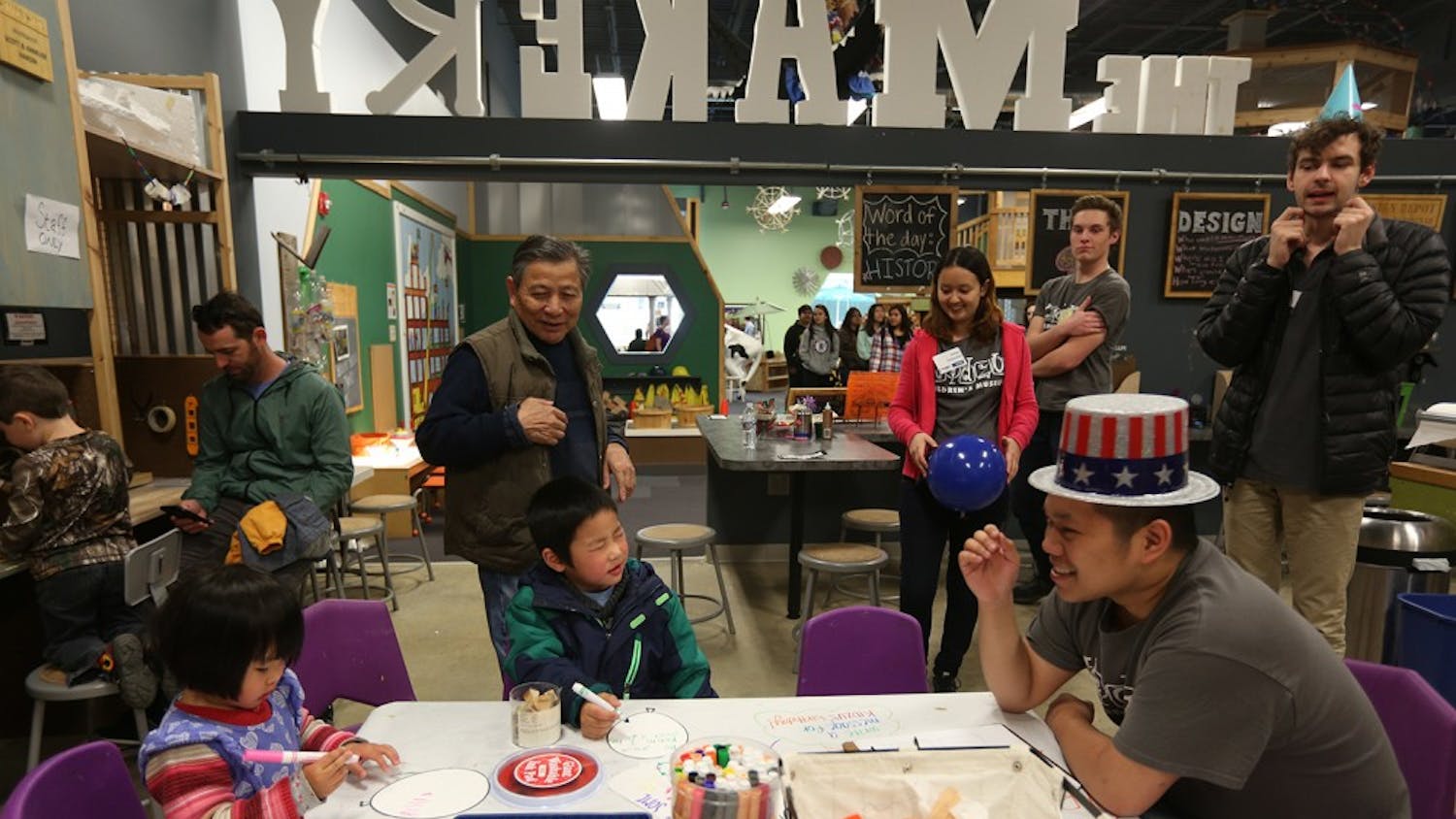 Kids do a coloring activity in celebration of Kidzu's 11th birthday as parents and counselors look on at University Mall on Sunday.