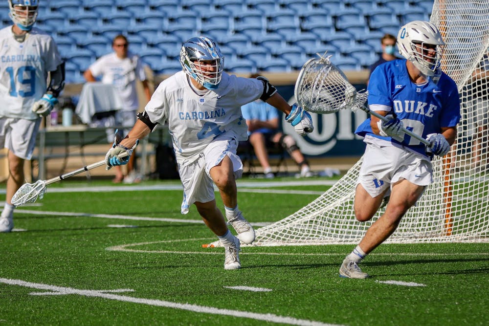 UNC senior attackman Chris Gray (4) attempts to regain possession from Duke graduate goalkeeper Mike Adler (0) during the Tar Heels' 15-12 victory against Duke on Sunday, May 2. With the victory, UNC and Duke share the 2021 ACC regular season title.