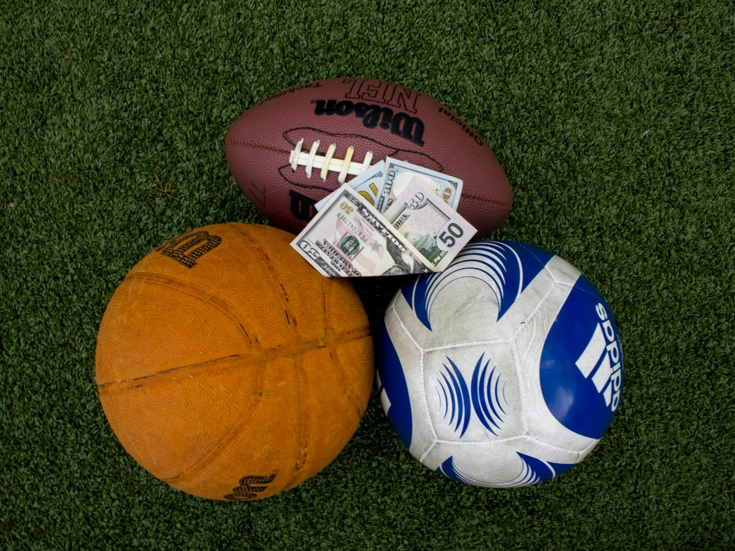 DTH Illustration. A bill is being proposed that will legalize sports betting for college and professional sports. Money lays on top of sports balls outside of Dorrance Field on Monday, March 27, 2023
