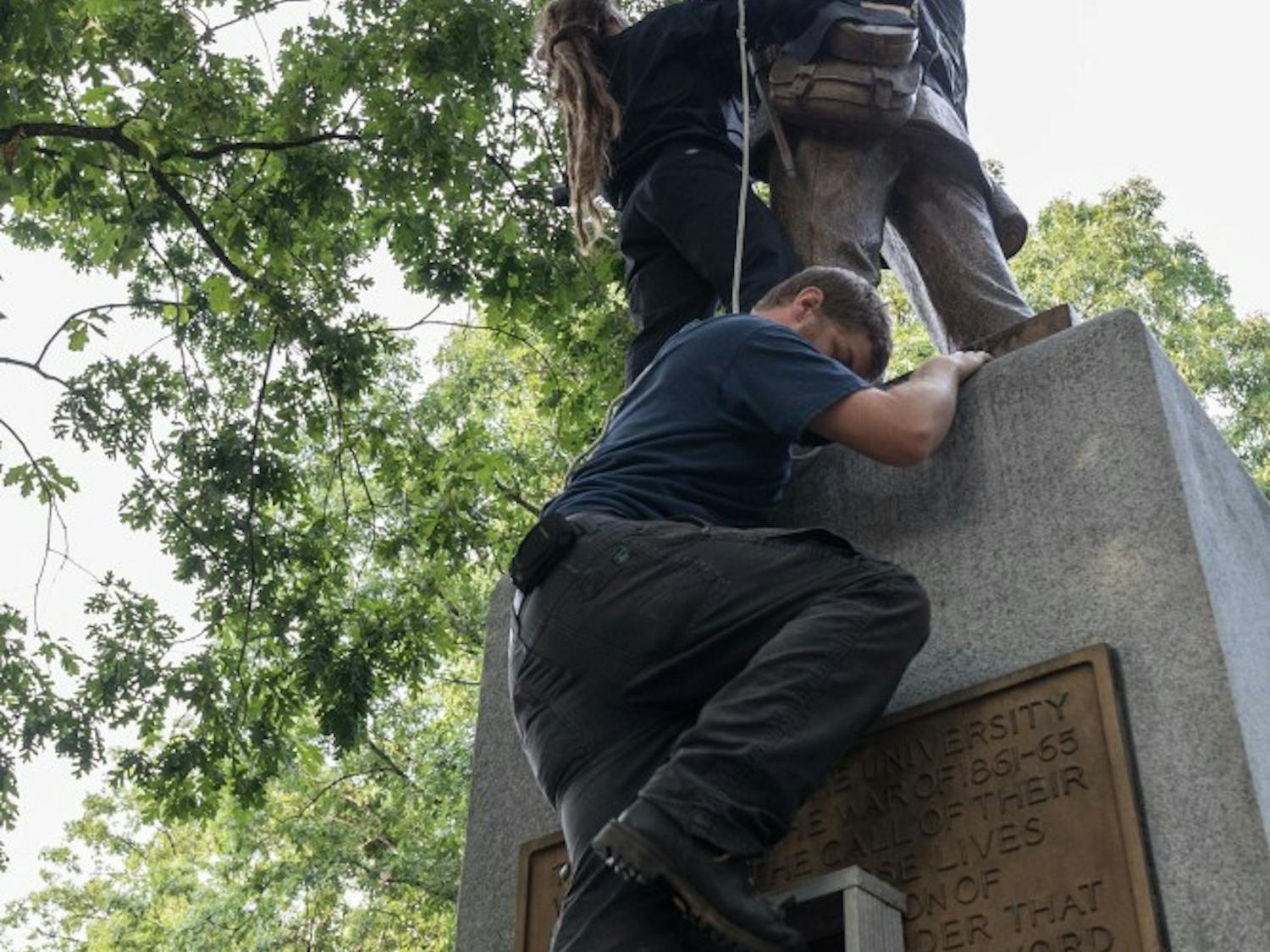Protesters climb Silent Sam to cover the statue with a black flag during Sunday's vigil.
