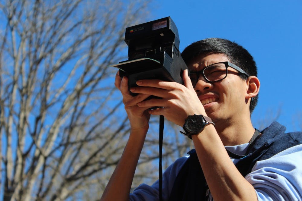Lucky Prachith, senior business major, uses his Polaroid camera at South Building on Tuesday, March 26, 2019. Prachith likes taking photos with his Polaroid camera because "it's a medium that's different in the sense that at the end of the day you get a tangible thing, it has a realness that separates it from digital photography." Pracith has been shooting with his Polaroid since his senior year of high school.