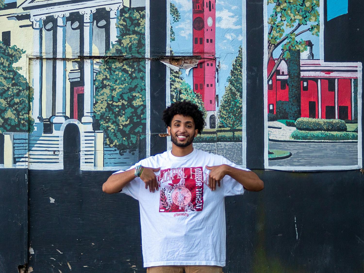 Eliam Mussie, the co-president of the Black Entrepreneur Initiative, pictured in front of the "Greetings from Chapel Hill" mural on Rosemary Street in Chapel Hill, N.C. on Tuesday, Sept. 6, 2022. Mussie is wearing a shirt from his clothing brand, Franklin Street Market, which will be represented at the pop-up this coming Saturday, Sept. 10, 2022.