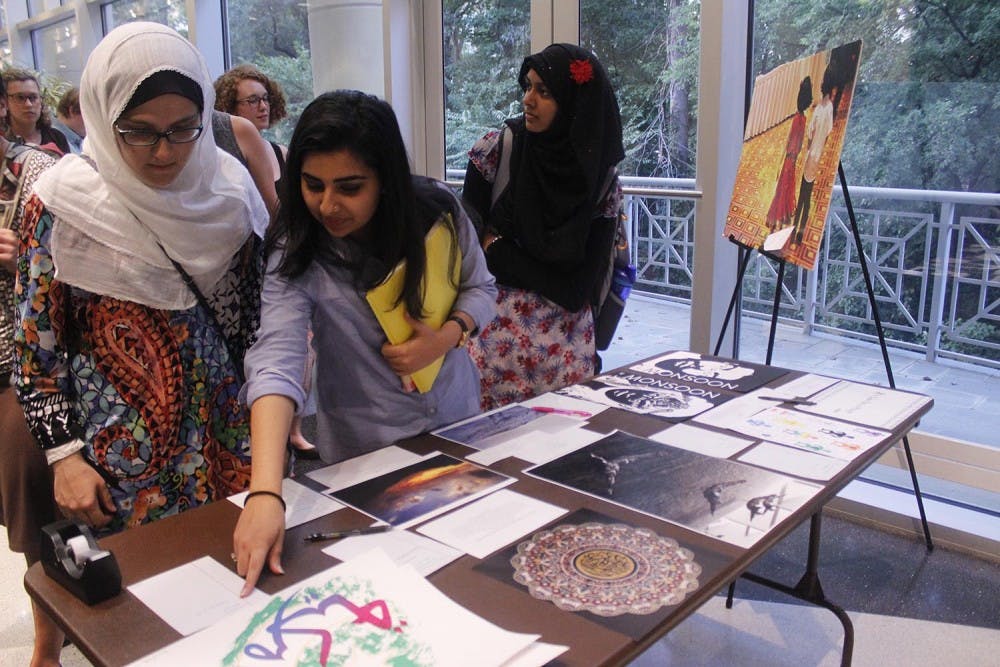 Soumaya Lansari (left), a junior global studies and sociology major, Ayesha Faisal (middle), a junior computer science major, and Safa Ahmed, a first-year media and journalism major look at art being auctioned at the Art and Welcoming Night on Tuesday. The proceeds from the auction will go to a fund for the victims of the Orlando shooting.