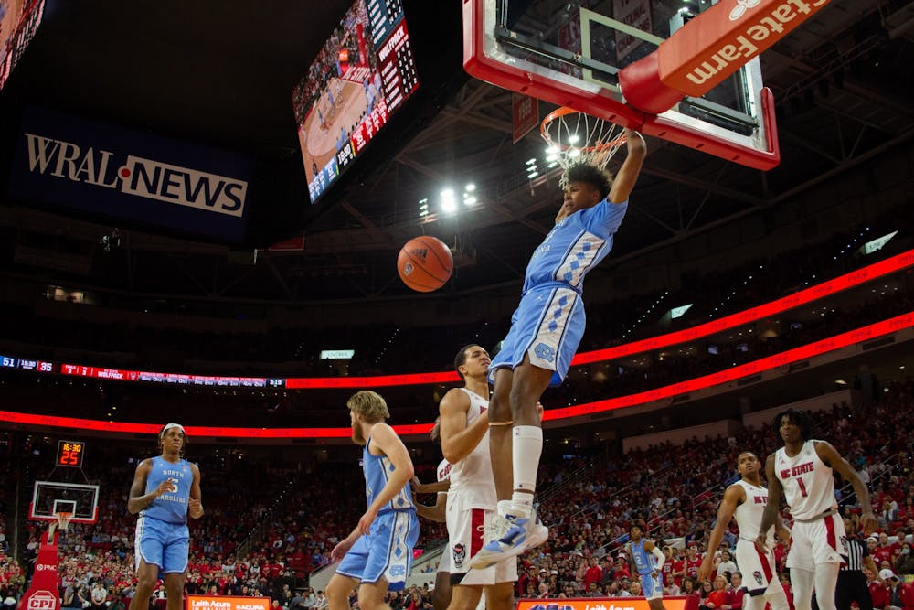 Sophomore guard Puff Johnson (14) hangs on the basketball hoop after a goal during UNC's rivalry game against NC State on Feb. 26, 2022. UNC won that game 84-74.