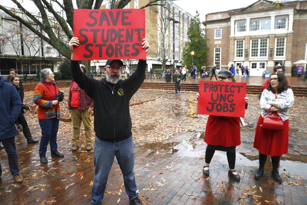 Former Student Stores employee Jason Adams (right) from Durham and Christina Pelech from Durham hold up signs to protest the privatization of Student Stores