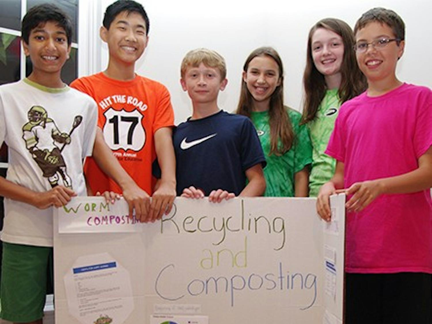 Middle School students stand in front of a compost bin and a poster displaying information on their compost and recycling project. Student names--ask Chloe. 