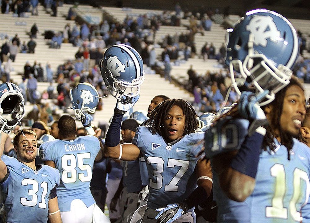 	North Carolina players Pete Mangum, T.J. Jiles and Tre Boston, from left to right, hold their helmets aloft during the fight song after the game, the team’s last of the season. 