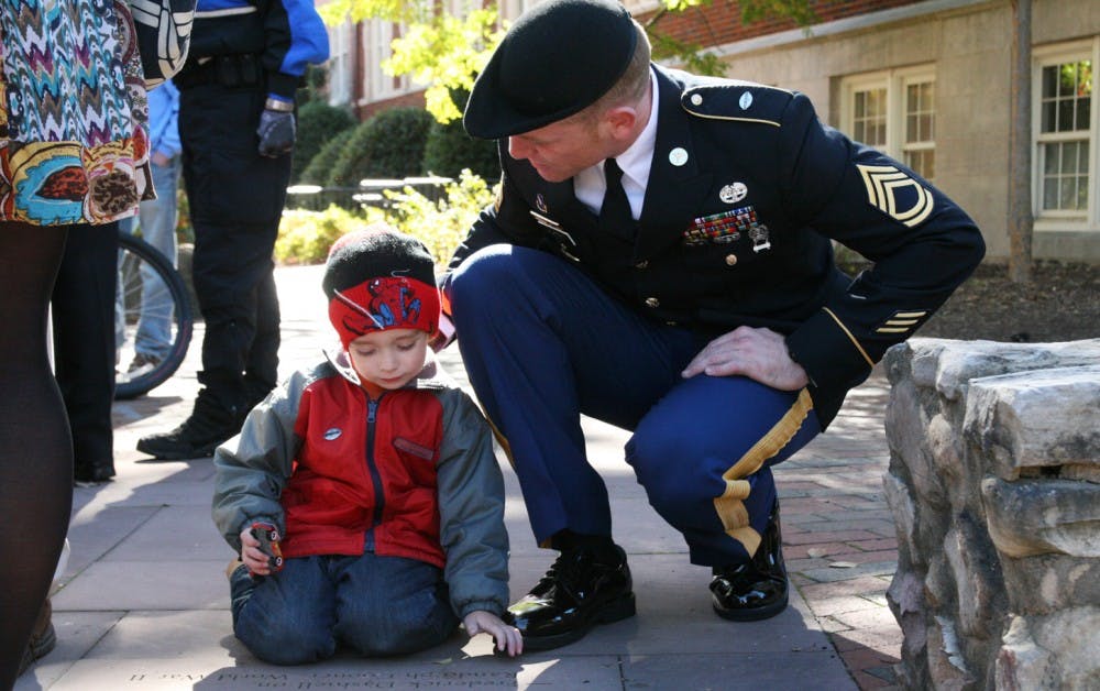 Army Sergeant First Class Sean P. Murphy kneels by his son Colin, 3, outside of Memorial Hall to read the inscriptions on the stones commemorating veterans.