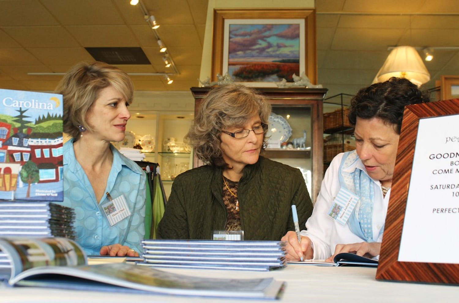 Elaine O'Neil, left, Marie Myers Lloyd and Missy Julian Fox sign copies of their book, Goodnight Carolina, at Peacock Alley Saturday morning. Marie and Missy wrote the book together while Elaine created the textile illustrations.