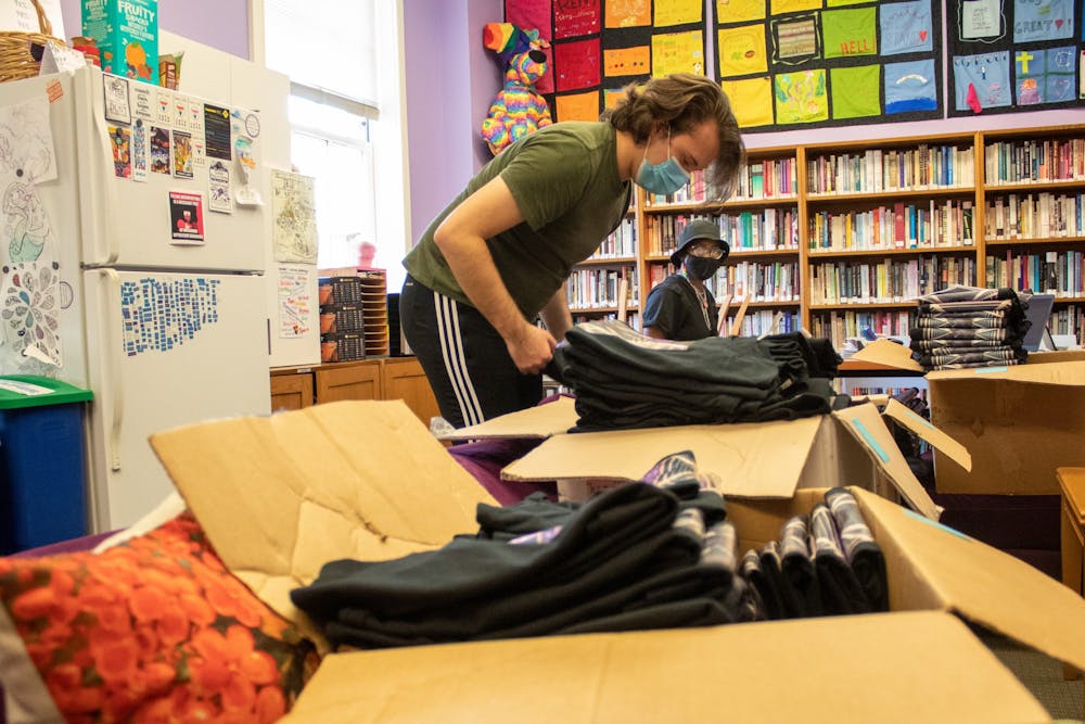 Nikalaus Ward, a student at the UNC LGBTQ Center, looks through boxes of specially designed new t-shirts that read "Imagine Liberation" for Pride Week, as Tiosa Iyamu folds zines.