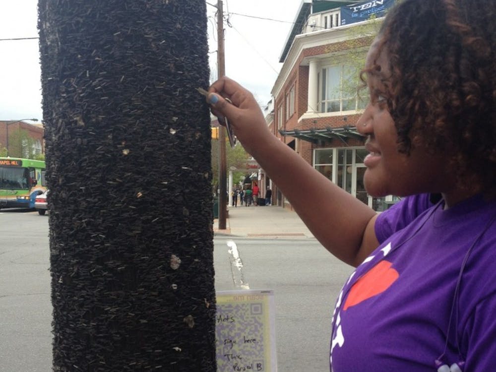 	Junior Mariah Monsanto attempts to remove a staple with her keys from the light post on the corner of S. Columbia and Franklin St.