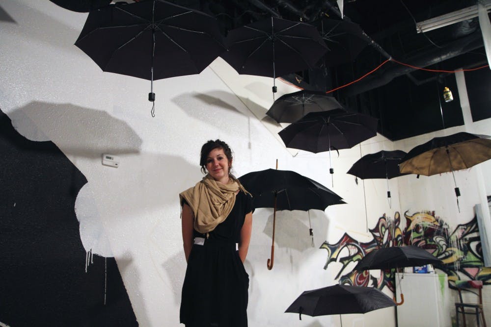 Molly Brewer stands beneath her umbrella exhibit at The Artery's <i>Work In Progress</i> opening. She was inspired to hang the umbrellas after many of her drawings were destroyed by a water leak.