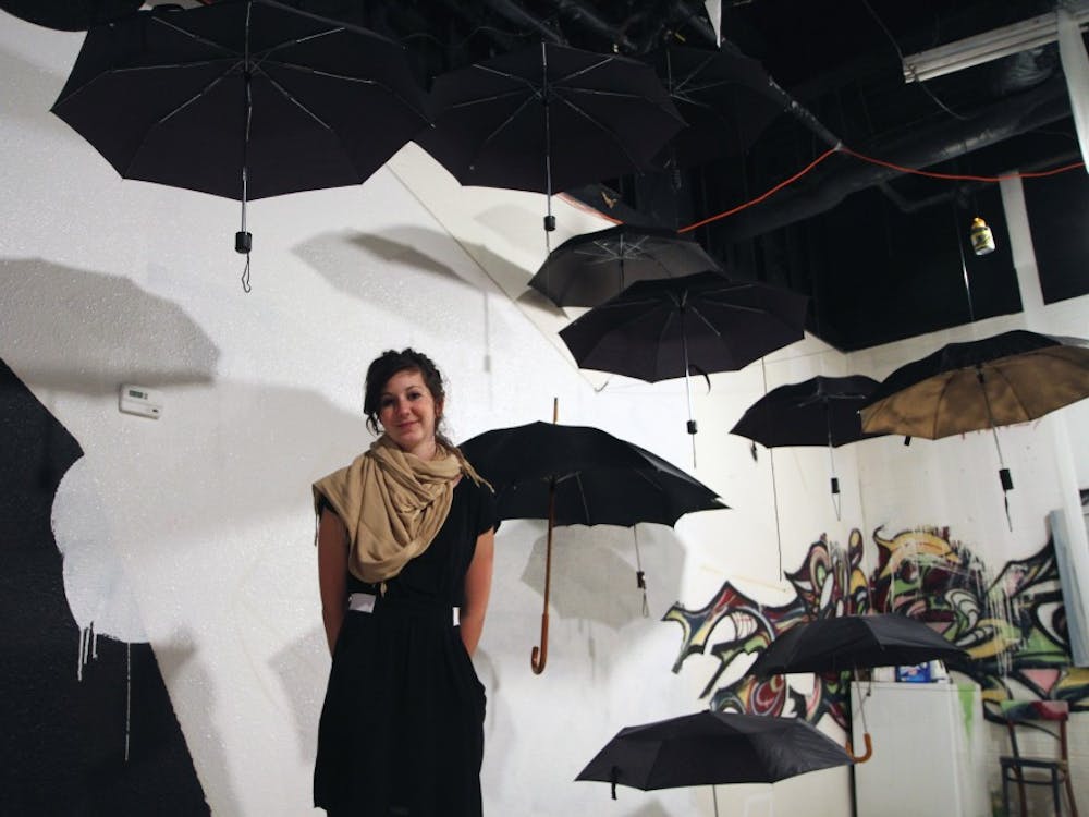 Molly Brewer stands beneath her umbrella exhibit at The Artery's Work In Progress opening. She was inspired to hang the umbrellas after many of her drawings were destroyed by a water leak.