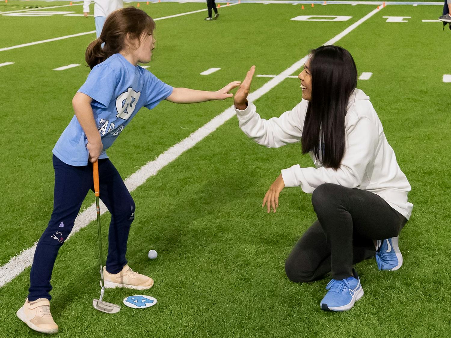 UNC first-year golfer Inez Ng high fives Sara Ludner at the National Girls & Women in Sports Day event held at the Bill Koman Practice on Sunday, Jan. 22, 2023.