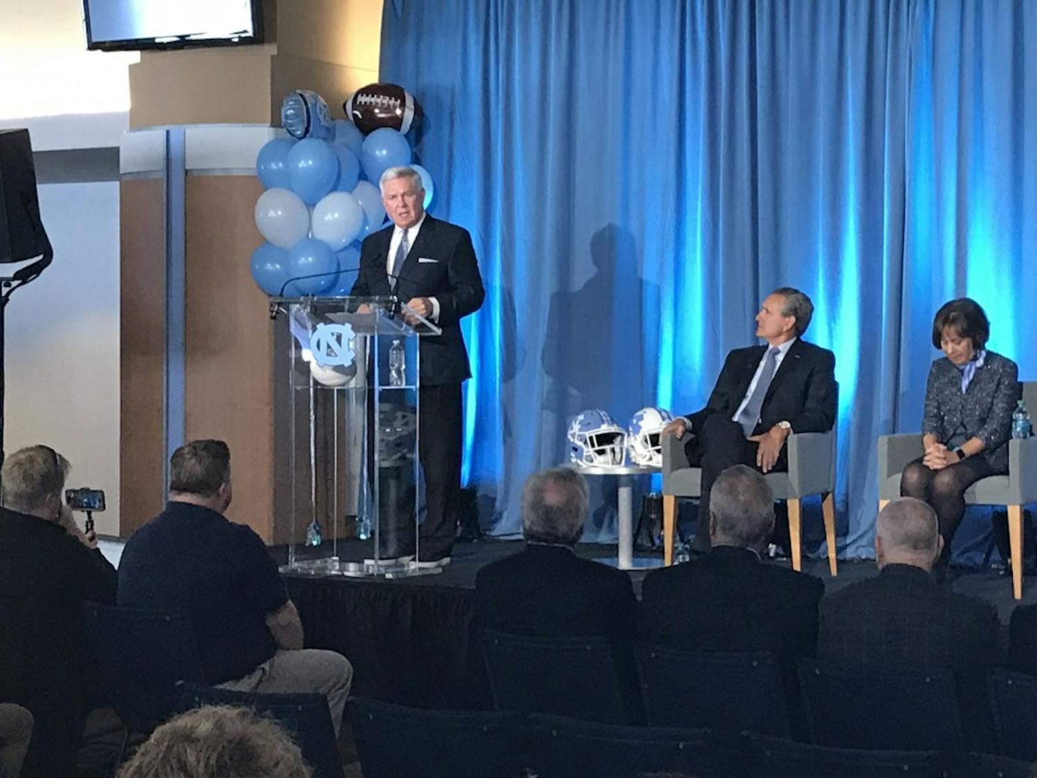 UNC head coach Mack Brown addresses the media at his introductory press conference on the third floor of the Loudermilk Center for Excellence on Nov. 27, 2018. Director of athletics Bubba Cunningham and Chancellor Carol Folt look on beside him.