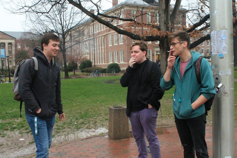 From left to right: UNC students Ethan Gilbreath, James Collette and Rory McFarlane smoke by the flagpole in Polk Place on Thursday afternoon.