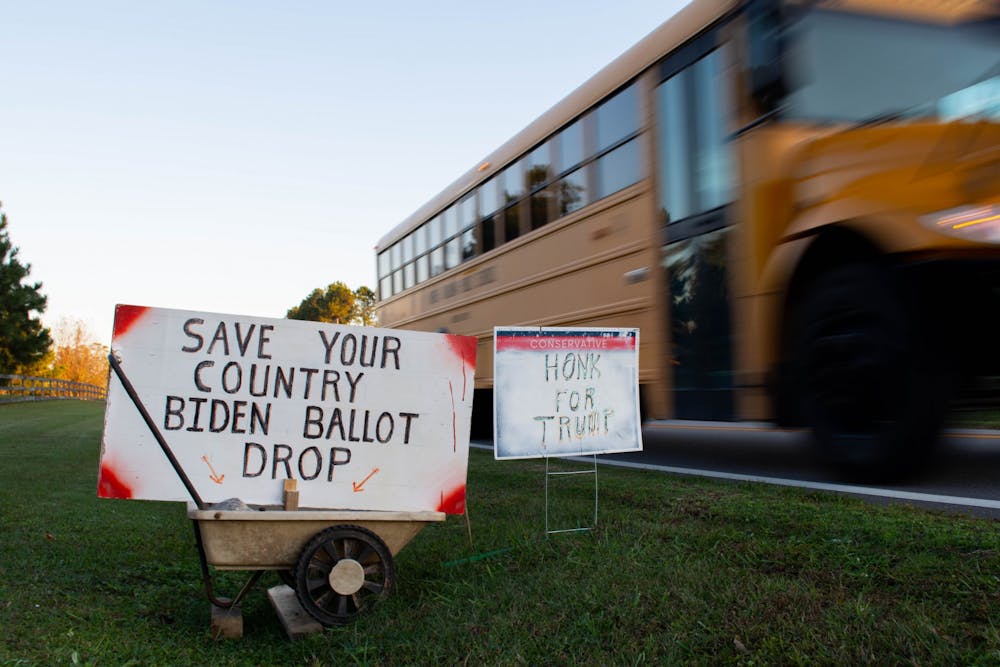 <p>A school bus passes by election signs in the yard of a Johnson County resident on Monday, Nov. 2, 2020. One sign encourages voters to "save their country" by throwing away ballots for Biden.&nbsp;</p>