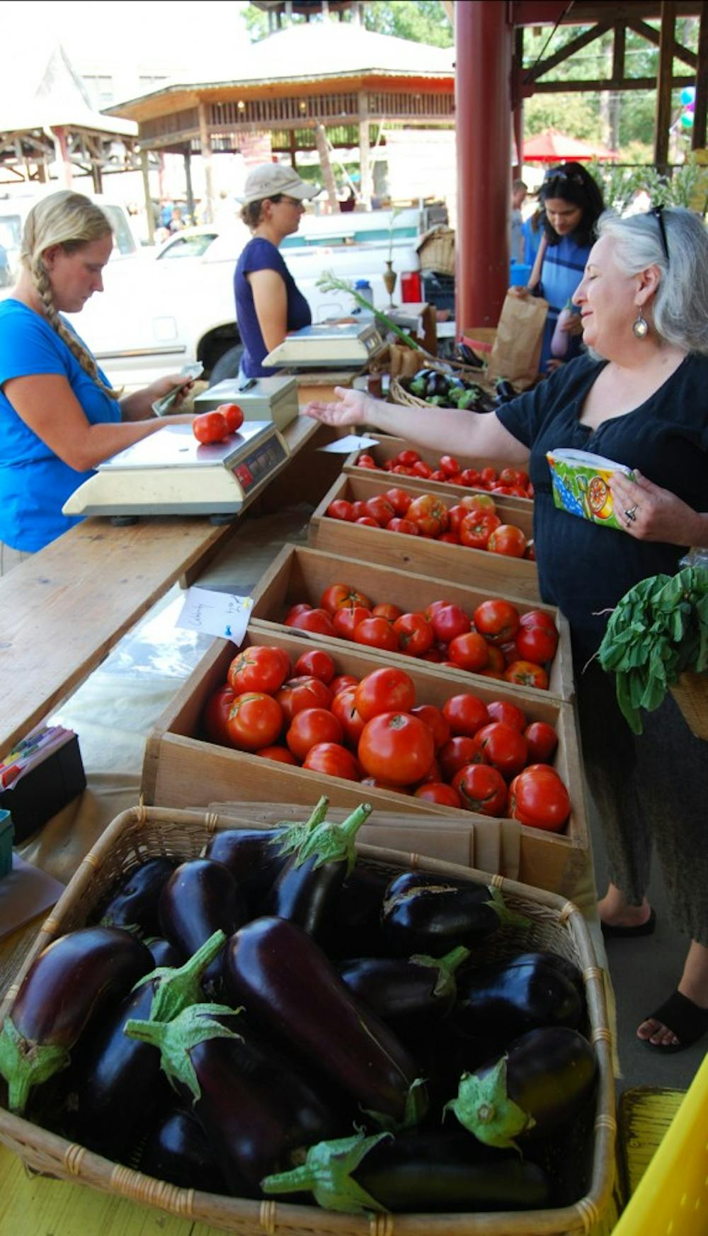Megan Cornett, an employee with Maple Spring Gardens in Cedar Grove, N.C., sells fresh tomatoes to a customer on Saturday morning. Maple Spring Gardens is one of the vendors that participated in the donation program to help homeless shelters and the needy, the Triangle Foodshare Challenge.
