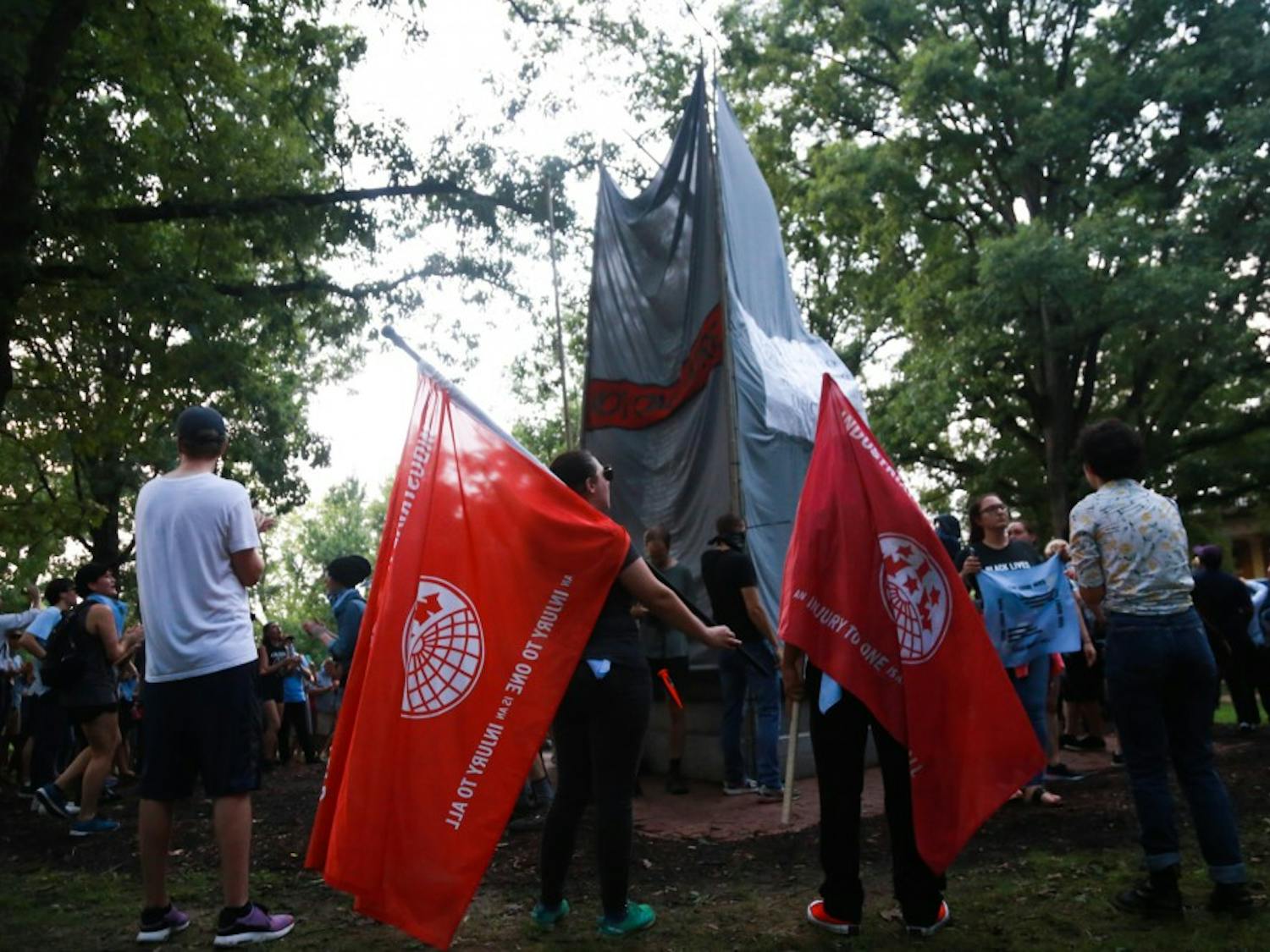 Rally attendees hold flags as other protesters tie banners around Silent Sam.