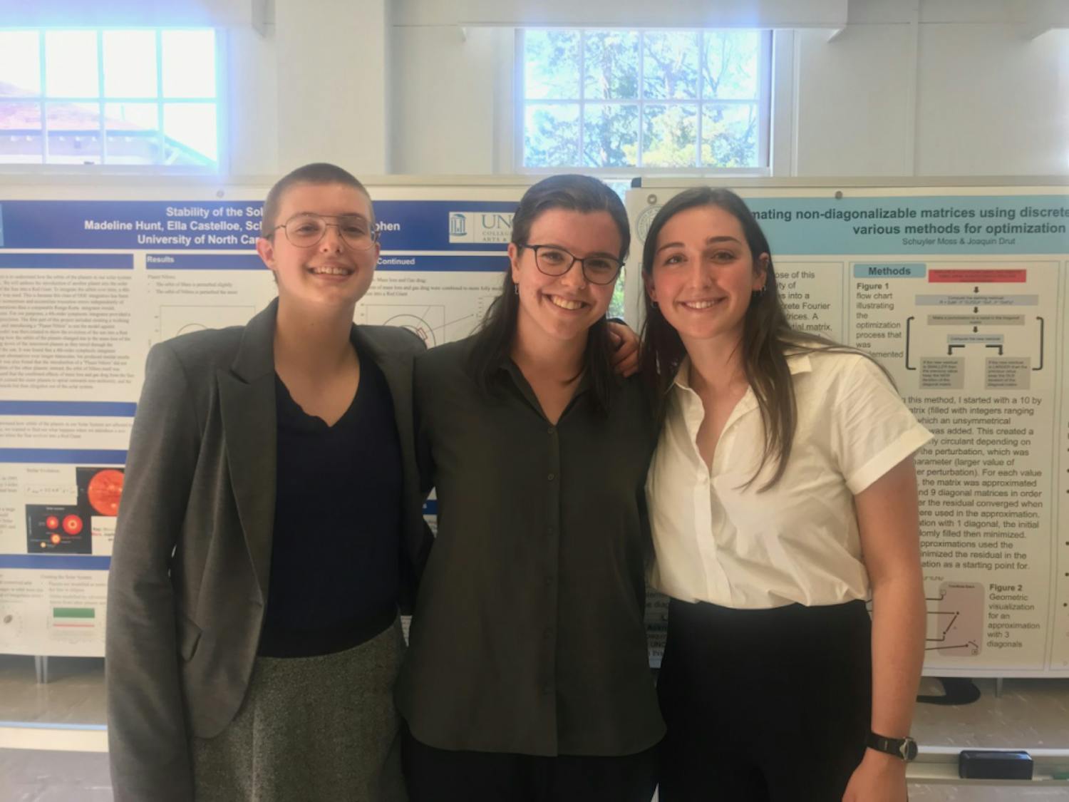 (Left to right) Madeline Hunt, Ella Castelloe and Schuyler Moss stand in front of their research projects at the Women in Physics Research Symposium.&nbsp;