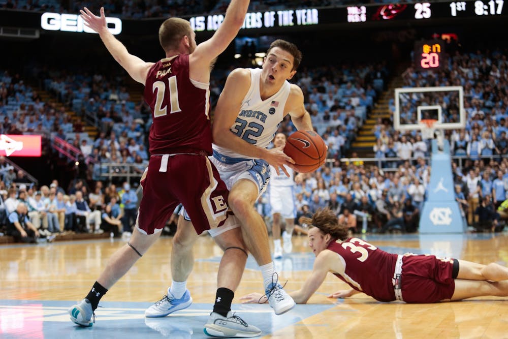 <p>UNC graduate forward Justin Pierce (32) attempts an offensive drive past Elon sophomore guard Andy Pack (21) and junior forward Simon Wright (33) during a game in the Smith Center on Wednesday, Nov. 20, 2019. The Tar Heels beat the Phoenixes 75-61.</p>