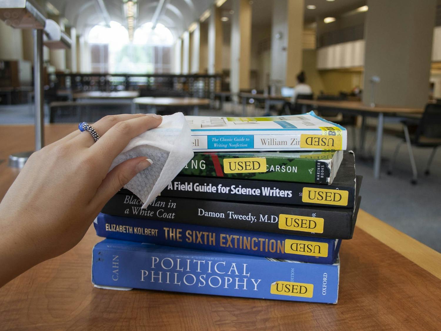 DTH Photo Illustration. A student wipes down books in Davis Library on Sunday, Aug. 16, 2020. UNC libraries are enforcing new protocols to prioritize the health and safety of library goers. 