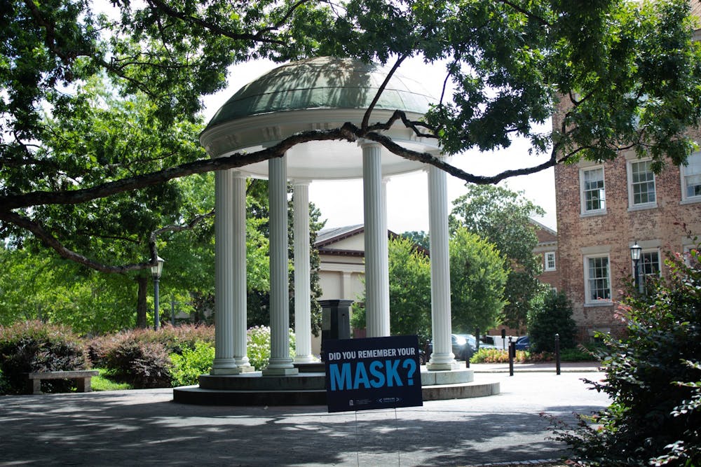 A sign reminding students and visitors to wear a mask sits near the Old Well on UNC's campus on Thursday, Aug. 13 2020. 