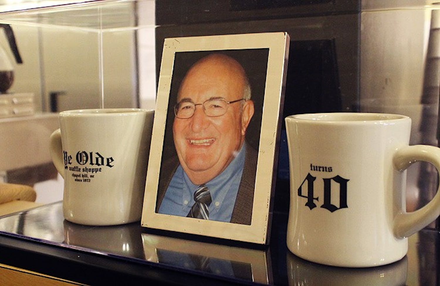 Ye Olde Waffle Shoppe will be celebrating its 40th anniversary tomorrow, with prices going back down to how they were in 1972. The Shoppe displays mugs they will be raffling off in commemoration of their anniversary, shown beside the owner. 