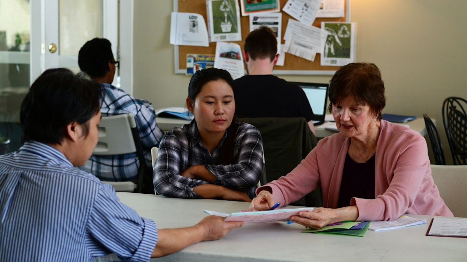 A refugee from Thailand (left) speaks with organizer Flicka Bateman (right) about papers while a translator (center) looks on. 