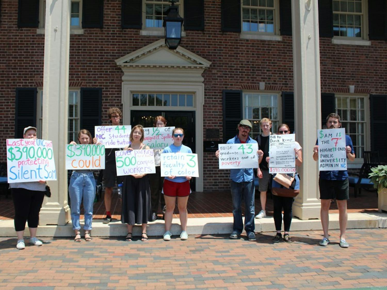 Protestors hold up signs in front of the Carolina Inn on July 18 protesting the Board of Trustees' expenditure on protecting Silent Sam. 