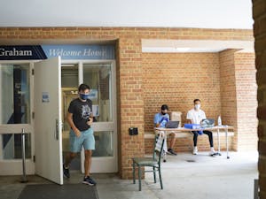 Tyler Smith, an incoming first-year, exits Graham Residence Hall wearing a mask as two RA's, sophomores Tiel Pham (left) and Nigel Goins (right) sit in the entryway to assist with move-in on Wednesday, Aug. 5, 2020.
