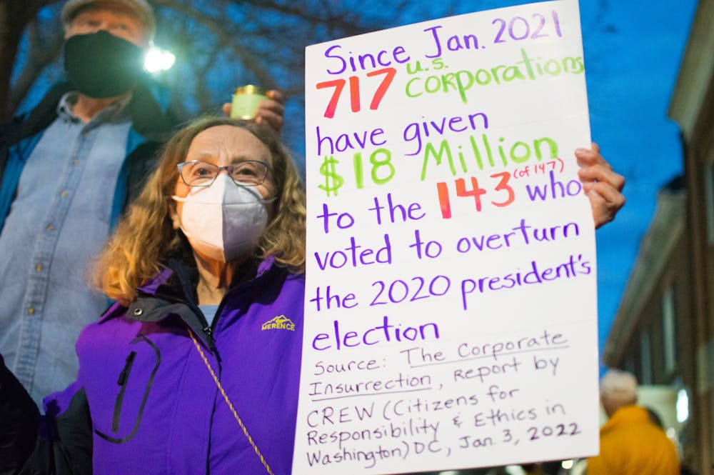 Chapel Hill resident Susan B. McClanahan holds a sign that calls out US corporations for their support of politicians who voted to overturn the 2020 presidential election. She holds the sign for passing by traffic at the candlelight vigil on Franklin Street on the one year anniversary of the attack on the US Capital on Jan 6, 2021.